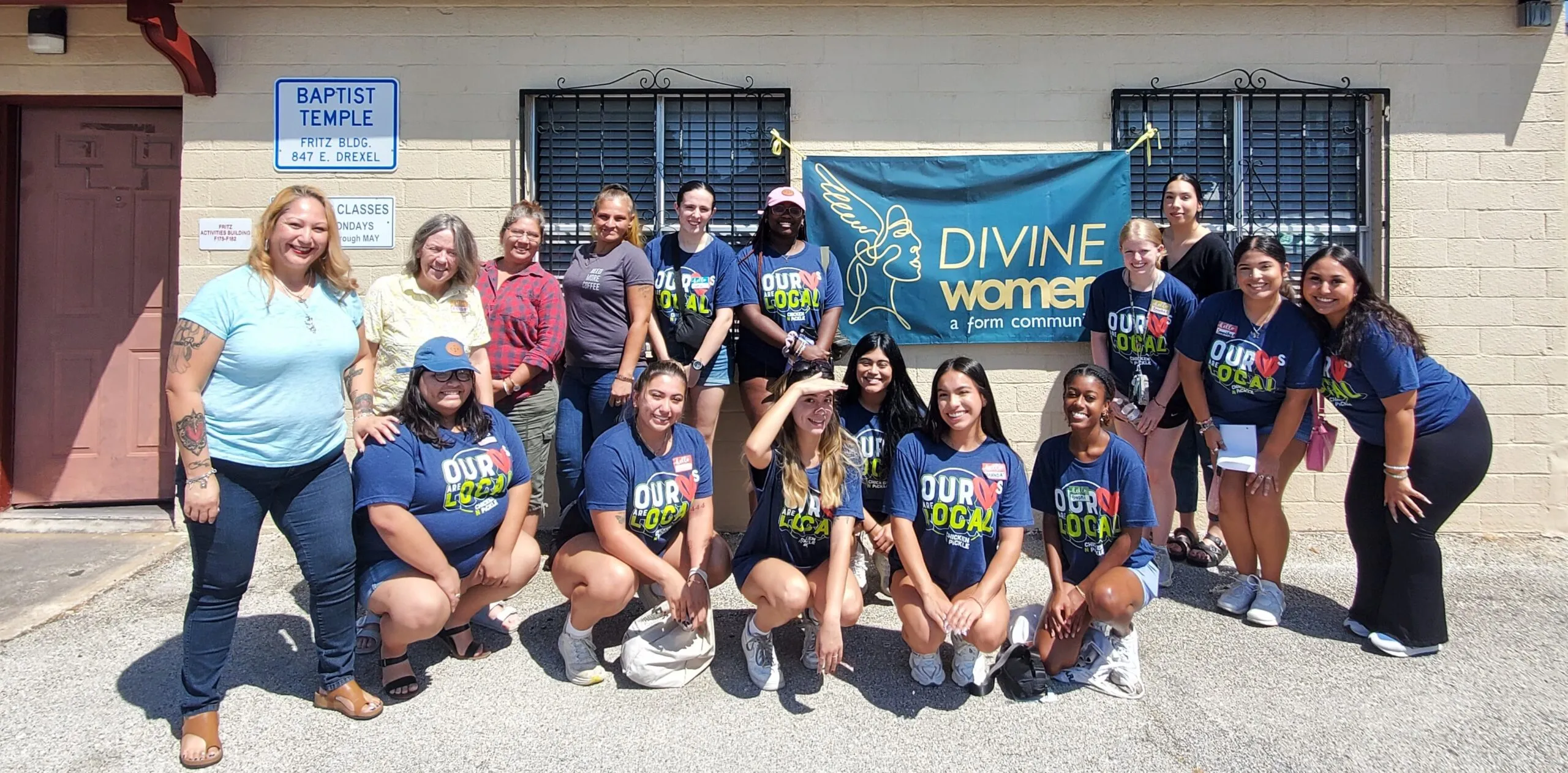 Integrantes de Divine Women con camisetas iguales, sonriendo juntas afuera frente a una manta de Divine Women