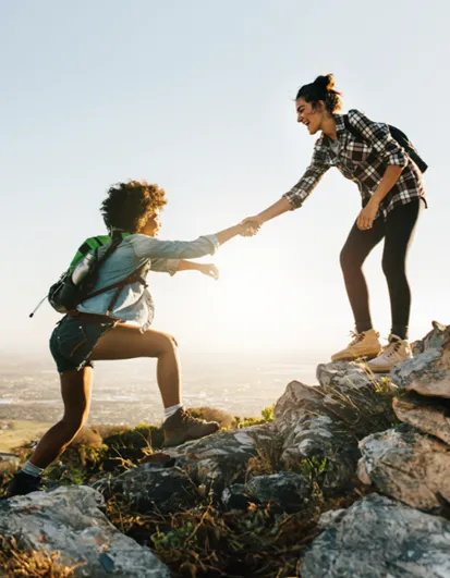 Dos mujeres de excursión; una ayuda a la otra a subir una roca